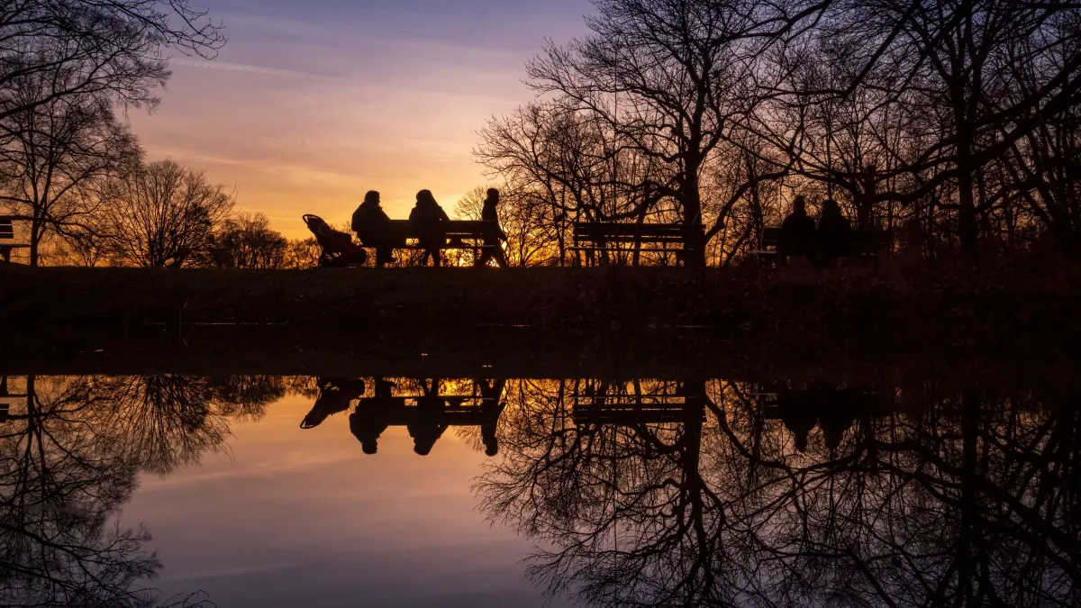 Ein Pärchen sitzt am Abend in der bayerischen Landeshauptstadt nahe eines spiegelglatten Baches im Englischen Garten. +++ dpa-Bildfunk +++
