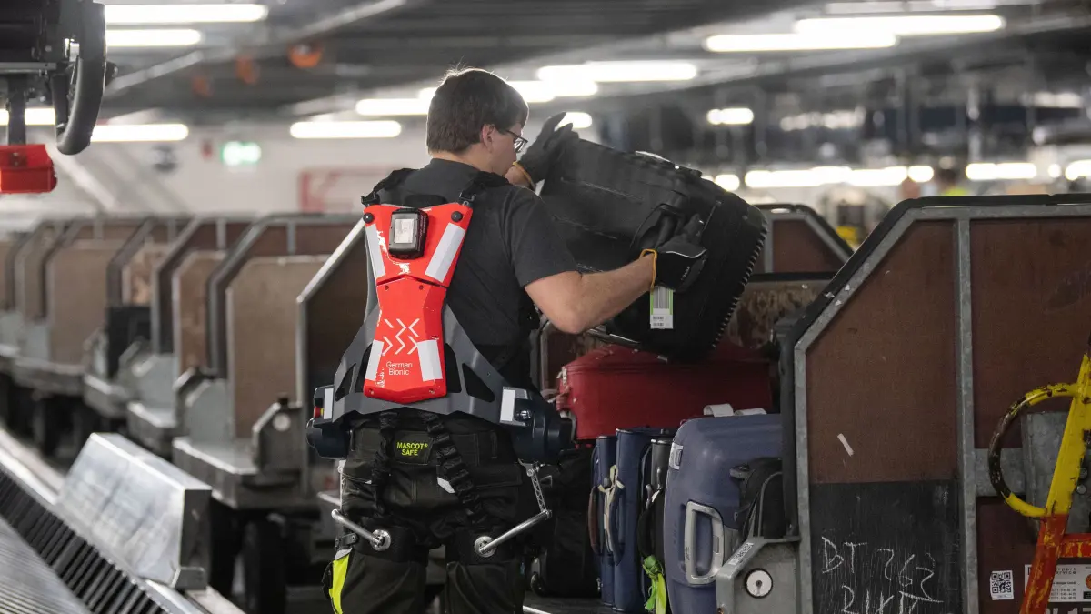 Ein Mitarbeiter des Stuttgarter Flughafens hebt mit Unterstützung eines Exoskeletts des Unternehmens German Bionic Systems in der Gepäckverteilung einen Koffer auf einen Gepäckwagen. Der Flughafen Stuttgart least zwei Exoskelette für je ein Jahr. Die Kraftanzüge sollen den Mitarbeitern beim Gepäck-Handling helfen, indem sie die Bewegungen der Träger unterstützen oder stärken. +++ dpa-Bildfunk +++