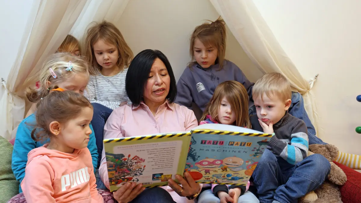 „Vorlesen passt in jeden Alltag!“: Eine Betreuerin liest in einer Kita den Kindern aus einem Buch vor Themenfoto vom 12.03.2024). Wer Kindern regelmaessig vorliest, staerkt ihre Sprachkompetenz, baut eine gute Beziehung zu ihnen auf und regt ihre Fantasie an. Dennoch liest laut dem aktuellen Vorlesemonitor der Stiftung Lesen rund ein Drittel aller Eltern ihren Kindern nur selten oder nie vor. Dabei gibt es kaum eine Beschaeftigung, die sich unkomplizierter in den Alltag einbauen laesst und bei richtiger Lektuere-Auswahl auch den Erwachsenen Spass macht, weiss die Leiterin Oldenburger Stadtbibliothek, Heike Janssen. Im Gespraech mit dem Evangelischen Pressedienst verraet die Mitorganisatorin der bundesweit fuehrenden Kinder- und Jugendbuchmesse Kibum, wie man bei den Kleinsten Begeisterung fuer Buecher weckt - und warum Lesen eher Ergaenzung als Konkurrenz zu digitalen Unterhaltungsangeboten ist. (Siehe epd-Gespraech vom 05.11.2024) *** Local Caption *** 00514185
