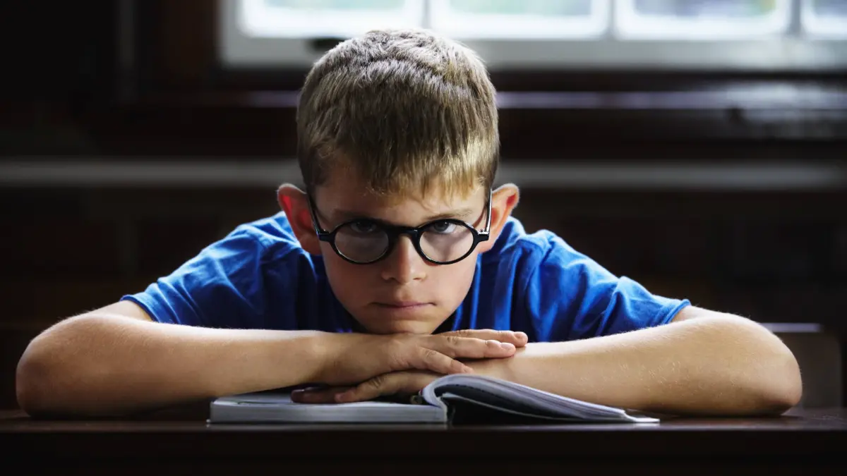 Kid, school and angry on desk, book and staring for education, adhd and child development. Anxiety, stress and burnout f: Kid, school and angry on desk, book and staring for education, adhd and child development. Anxiety, stress and burnout from dyslexia, moody or mental health issue for studying, frustrated and autism. model released / property released Copyright: xwww.peopleimages.comx