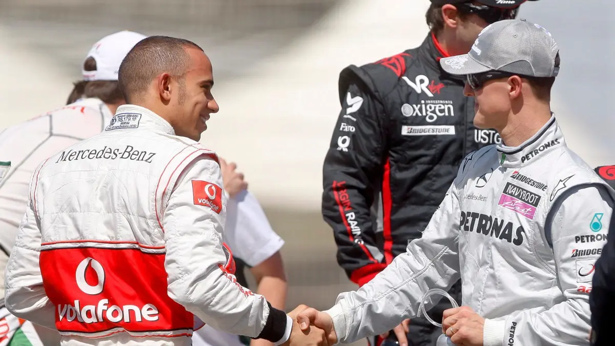 Lewis Hamilton (l) und Michael Schumacher: ARCHIV - 13.03.2010, Bahrain, Sakhir: Der britische Formel-1-Pilot Lewis Hamilton (l) und Michael Schumacher aus Deutschland begrüßen sich am 14. März 2010 vor dem Gruppenfoto auf dem Bahrain International Circuit in Sakhir. (zu dpa: «Hamiltons bewegende Worte zum Schumacher-Vermächtnis») Foto: Diego Azubel/dpa +++ dpa-Bildfunk +++