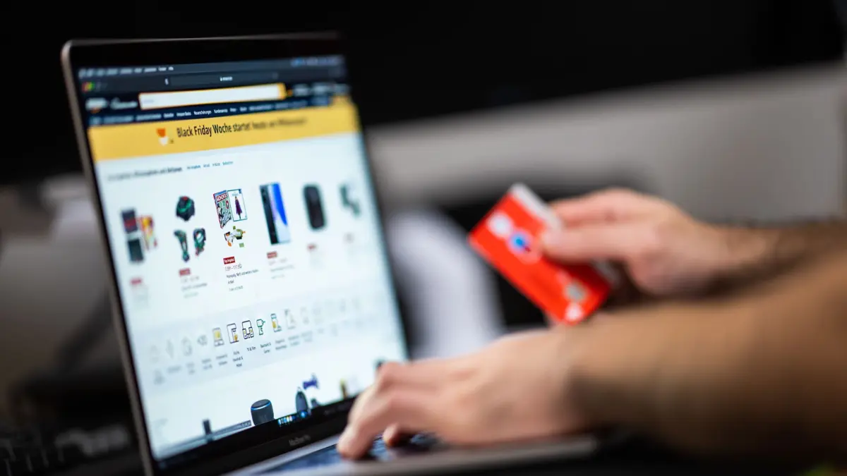 ARCHIV - 18.11.2021, Niedersachsen, Oldenburg: Ein Mann mit einer Bankkarte in der Hand sitzt am Laptop und schaut sich die Black Friday Angebote auf der Online-Shopping-Seite von Amazon an. Bei Männern ist die Schnäppchenjagd an den Tagen rund um den Black Friday einer Umfrage zufolge deutlich beliebter als bei Frauen. (zu dpa «Umfrage: Männer beim Black Friday kauffreudiger als Frauen») Foto: Mohssen Assanimoghaddam/dpa +++ dpa-Bildfunk +++