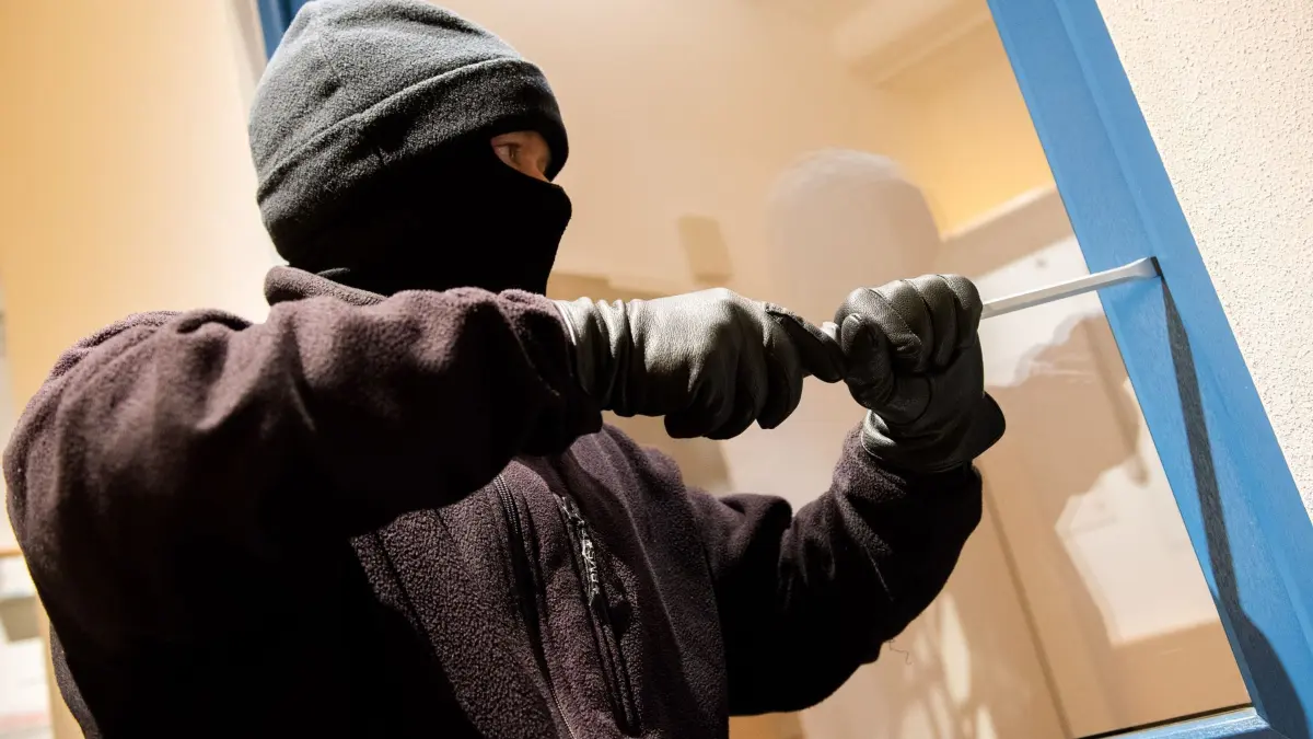 Polizei demonstriert das Vorgehen eines Einbrechers: ARCHIV - 28.06.2016, Nordrhein-Westfalen, Hamburg: Ein als Einbrecher verkleideter Mann hebelt in einer Kriminalpolizeilichen Beratungsstelle der Polizei ein Fenster auf. (zu dpa: «Abhör-Erlaubnis bei Wohnungseinbrüchen verlängert») Foto: Daniel Bockwoldt/dpa +++ dpa-Bildfunk +++