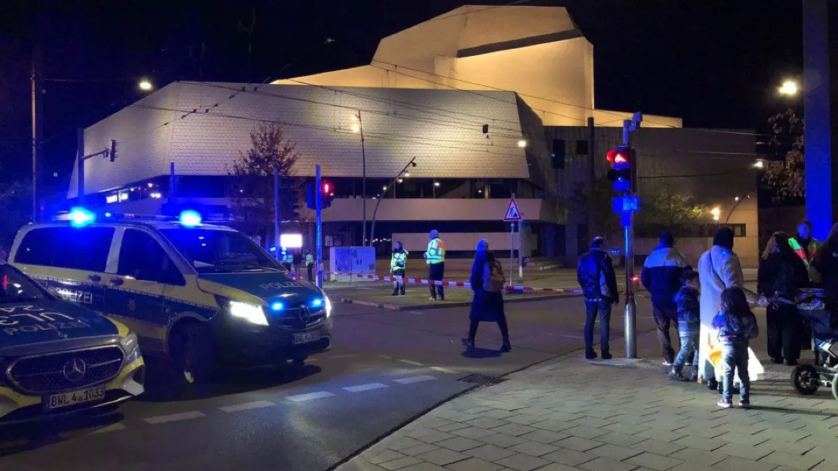 Am Theater warten 10 bis 15 Menschen an den Absperrbändern der Polizei.Rui aus Aachen wäre eigentlich über Nacht im Ibis-Hotel. Er hat seinen Koffer bei sich und sagt: „Wir durften gerade noch unsere Sachen holen und mussten dann das Hotel verlassen.“