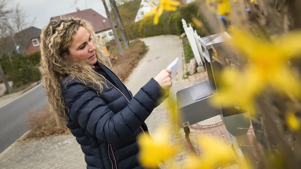 Eine Frau liest Post vor dem Briefkasten: ILLUSTRATION - Ein genauer Blick auf die Rechnung hilft: Ist der Beitrag gestiegen, könnte eine Kündigung sinnvoll sein. (zu dpa: «Kfz-Versicherung: So können Sie noch nach der Frist kündigen») Foto: Christin Klose/dpa-mag - Honorarfrei nur für Bezieher des Dienstes dpa-Magazin +++ dpa-Magazin +++
