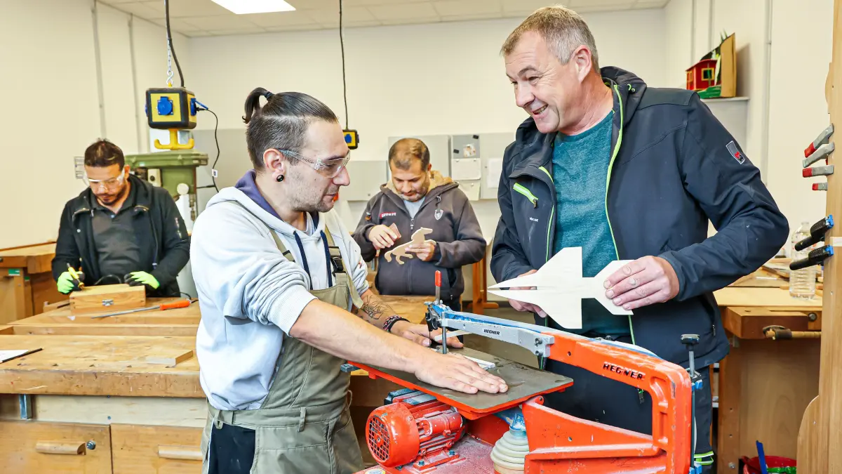 Jürgen Wengert (rechts), pädagogischer Anleiter bei der inab in Sulzdorf, erläutert Teilnehmer Christian Samardzija, wie er die Teile für das Holzflugzeug sägen muss.