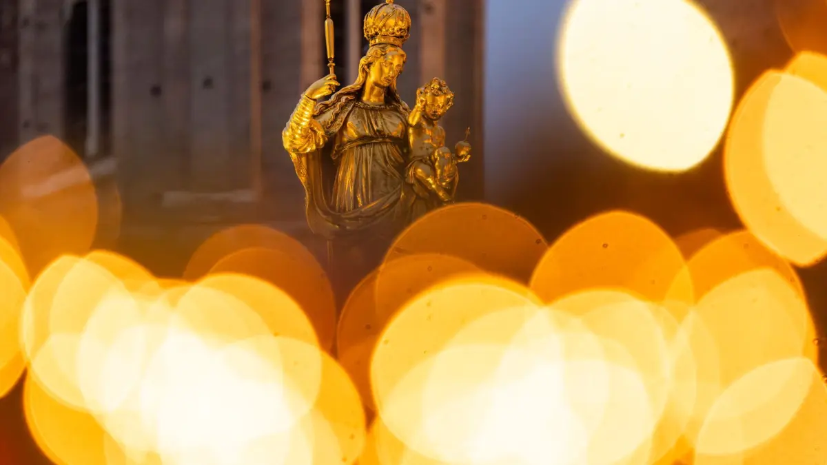 Marienfigur im Weihnachtslicht: 11.12.2024, Bayern, München: Eine goldene Marienfigur steht auf dem Marienplatz im Licht des umliegenden Weihnachtsmarkts. Der Platz liegt im Zentrum der Stadt. Foto: Peter Kneffel/dpa +++ dpa-Bildfunk +++