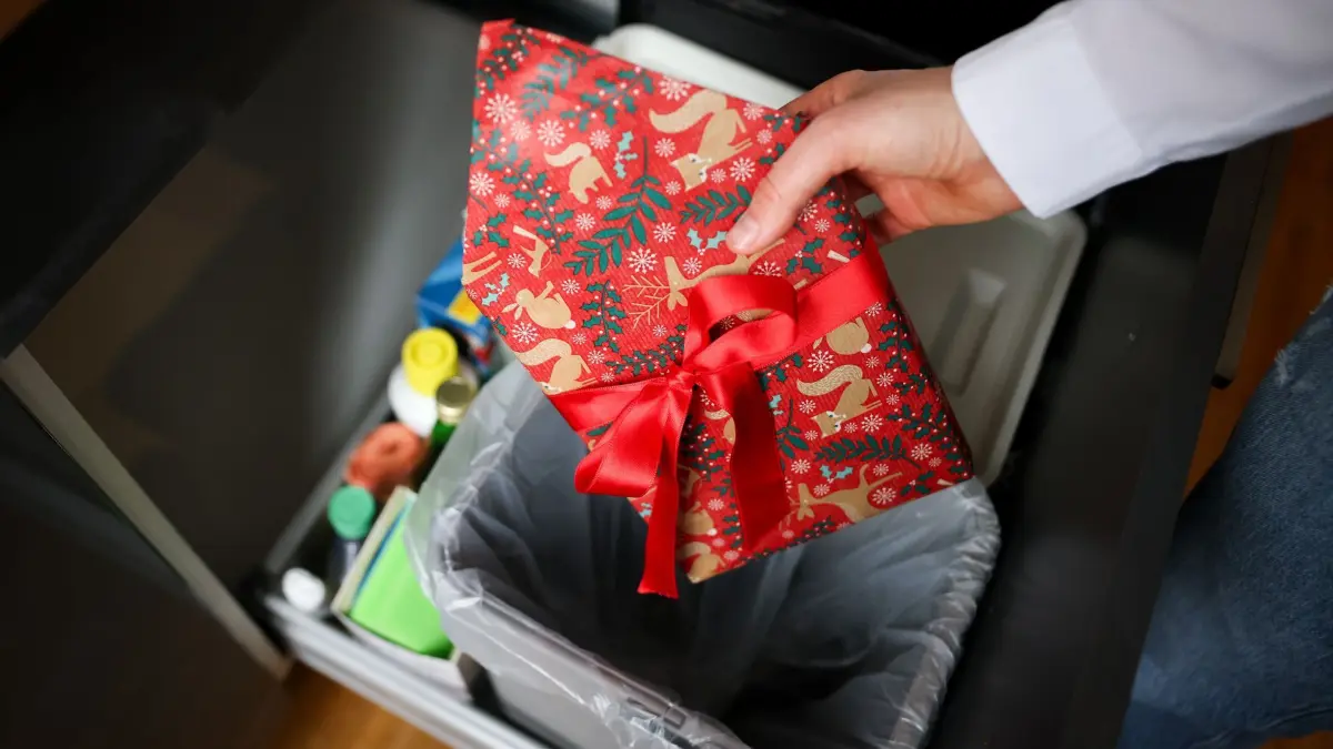 Weihnachtsgeschenke: ILLUSTRATION - 07.12.2024, Hamburg: Eine Frau wirft ein weihnachtlich verpacktes Geschenk in den Mülleimer (Gestellte Szene). (zu dpa: «Umfrage: Schwiegereltern liegen bei Geschenken oft richtig») Foto: Christian Charisius/dpa +++ dpa-Bildfunk +++