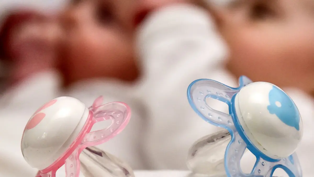 ARCHIV - 13.04.2015, Brandenburg, Frankfurt (Oder): Ein rosa und ein blauer Schnuller, aufgenommen am 14.04.2015 vor zwei Babys in Frankfurt (Oder) in Brandenburg. In Hamburg wurde zu Neujahr ein Zwillingspaar geboren. (zu dpa: «Henry und Theo: Zwillingsglück zum Jahresbeginn») Foto: Patrick Pleul/dpa +++ dpa-Bildfunk +++