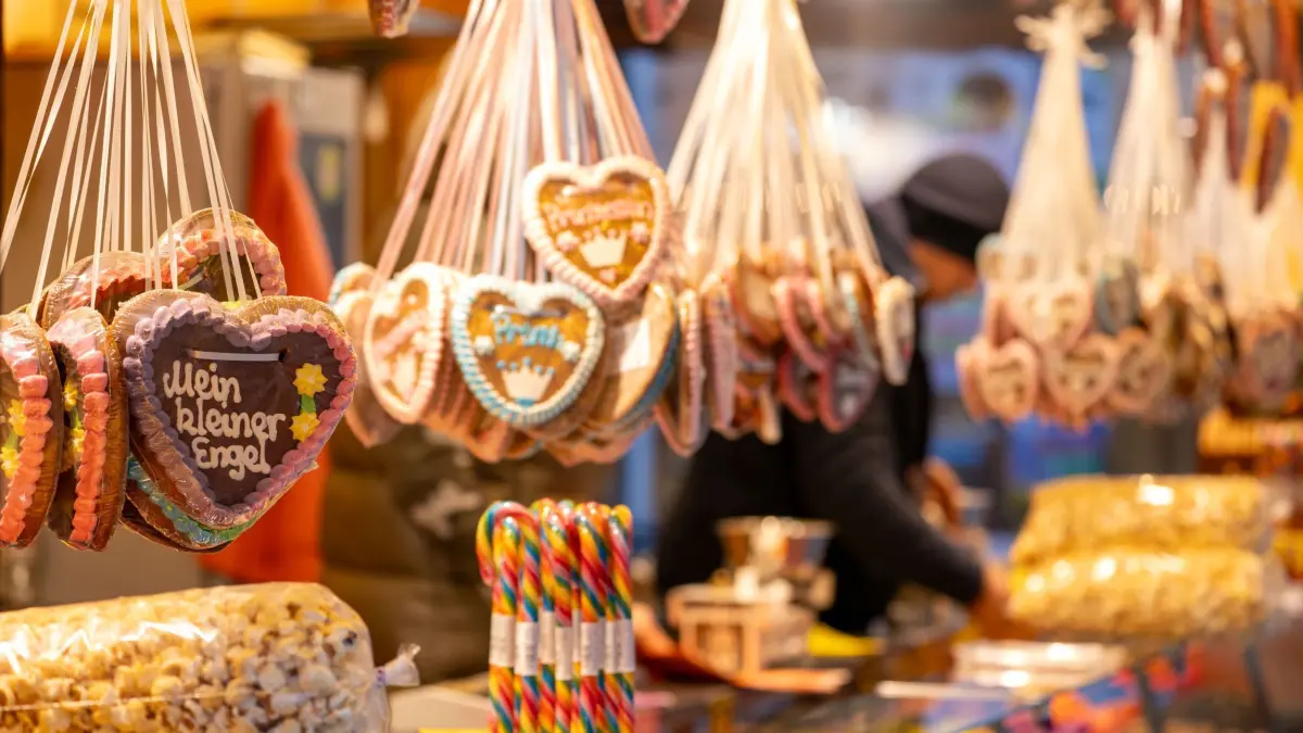 Weihnachtsmarkt: ARCHIV - 10.11.2024, Bayern, Bayreuth: Die Aufschrift "Mein kleiner Engel" ist auf einem Lebkuchenherz zu lesen, im Hintergrund packt ein Verkäufer eine Tüte mit Süßigkeiten. Das Bayreuther Winterdorf verbreitet bereits vor dem Aufbau des offiziellen Weihnachtsmarktes weihnachtliche Stimmung. (zu dpa: «Alkohol, Süßes und Fleisch: Ladenhüter nach dem Fest») Foto: Pia Bayer/dpa +++ dpa-Bildfunk +++