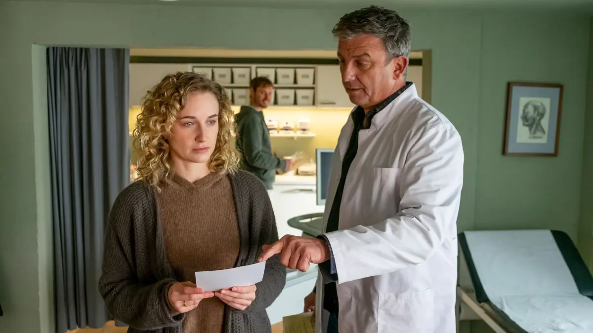 Dr. Martin Gruber (Hans Sigl, r.) hat für seine Patientin Jana Weiss (Pia Barucki, l.) gute Nachrichten: Sie ist schwanger. Doch ihre Freude ist verhalten, was auch David Ka?stner (Fre?de?ric Brossier, M.) irritiert.