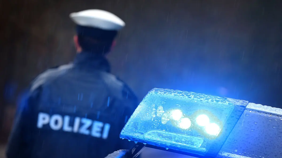 ARCHIV - 15.03.2019, Bayern, Kempten: ILLUSTRATION - Ein Polizist steht im Regen vor einem Streifenwagen dessen Blaulicht aktiviert ist. Eine junge Frau soll einen vier Jahre alten Bub in Eschenbach in der Oberpfalz mit Gewalt getötet haben. Sie sitze wegen des Verdachts des Totschlags in Untersuchungshaft, teilte die Polizei am Freitag mit. Foto: Karl-Josef Hildenbrand/dpa +++ dpa-Bildfunk +++