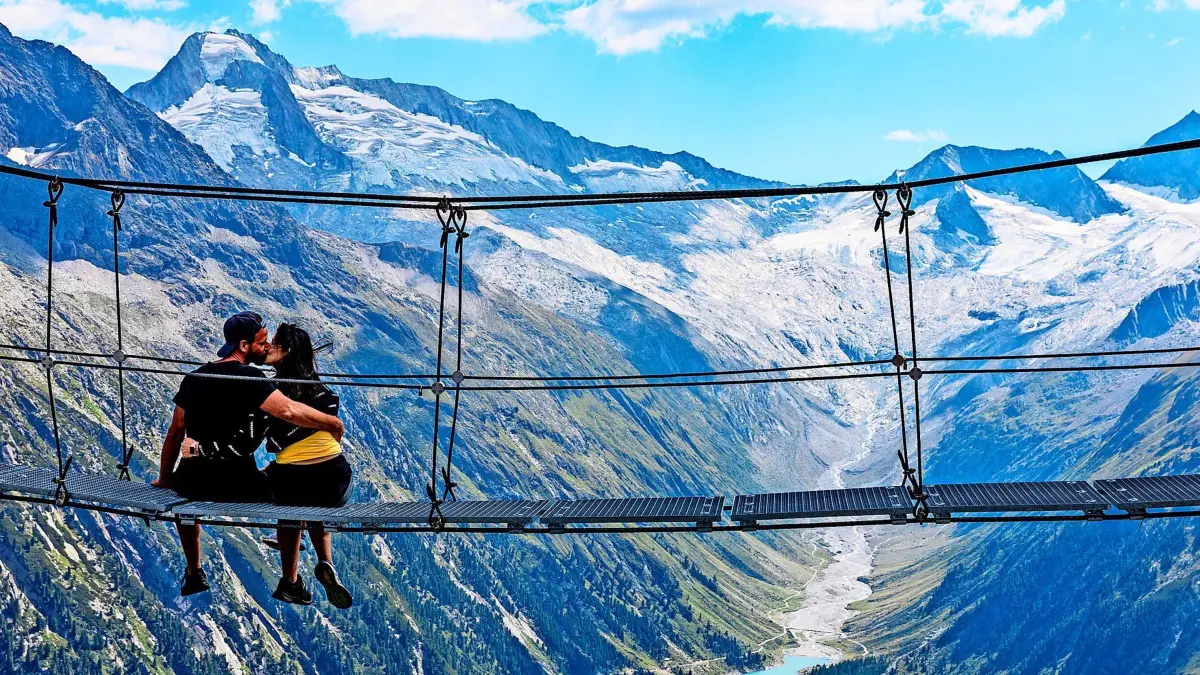 ARCHIV - 19.08.2023, Österreich, Zillertaler Alpen: Eine Frau und ein Mann küssen sich auf einer Hängebrücke an einem Wanderweg in den Zillertaler Alpen - mit Blick auf den Schlegeis-Speicher und die umgebenden Alpengipfel. (zu dpa: «Auf nach Österreich: Tourismus verbucht Rekord») Foto: Frank Hammerschmidt/dpa +++ dpa-Bildfunk +++