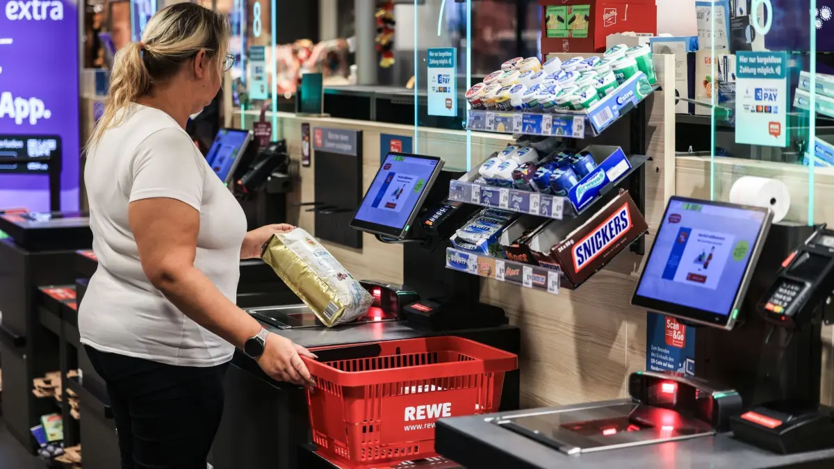 Rewe - Selbstbedienungskasse: ARCHIV - 03.07.2024, Nordrhein-Westfalen, Köln: Eine Frau scannt in einer Rewe-Fliale ein Produkt an einer Selbstbedienungskasse. (zu dpa: «Händler sichern ihre SB-Kassen mit Künstlicher Intelligenz») Foto: Oliver Berg/dpa +++ dpa-Bildfunk +++