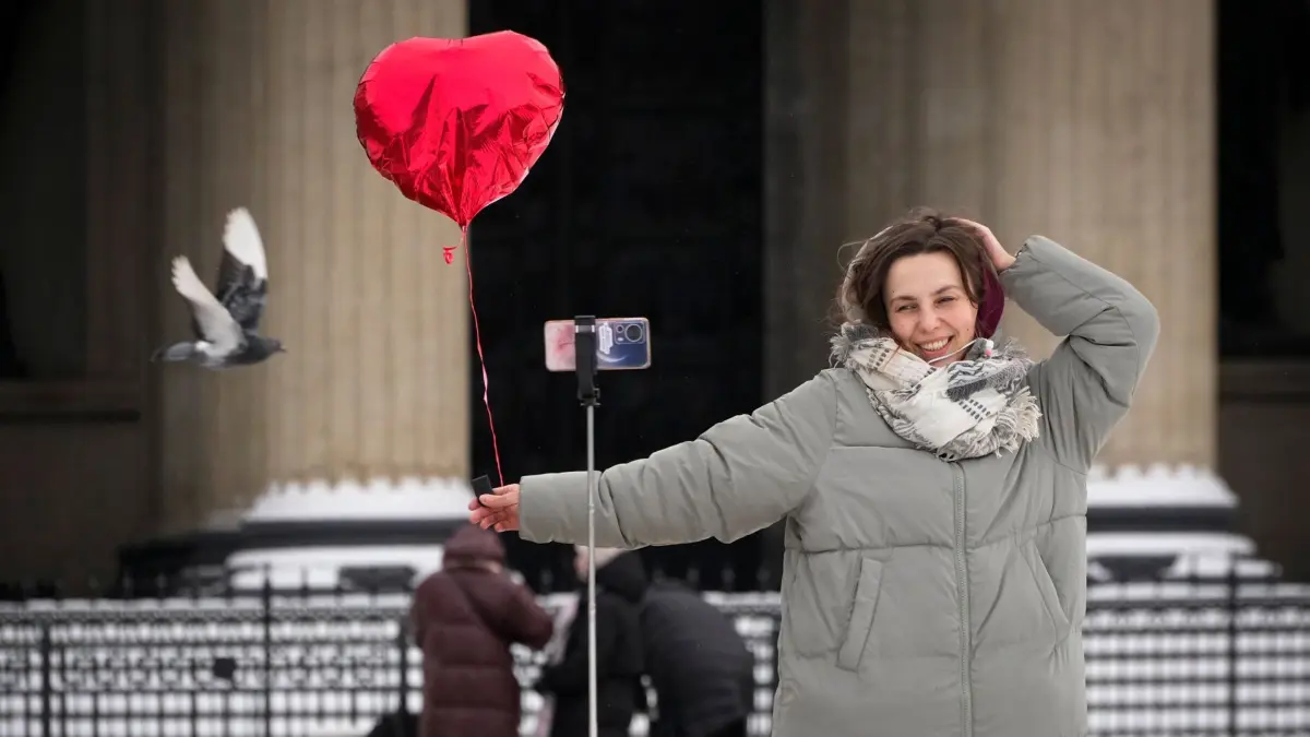 Valentinstag in St. Petersburg: 14.02.2025, Russland, St. Petersburg: Eine Frau filmt sich mit einem Smartphone am Valentinstag und hält einen Herzluftballon in der Hand. Foto: Dmitri Lovetsky/AP/dpa +++ dpa-Bildfunk +++