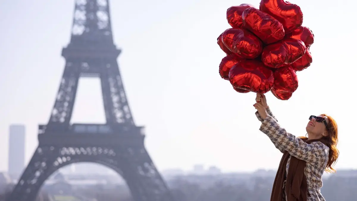 Valentinstag in Paris: 14.02.2025, Frankreich, Paris: TOPSHOT - Eine Frau hält am Valentinstag gegenüber dem Eiffelturm an der Seine rote herzförmige Luftballons in die Höhe. Foto: Ian Langsdon/AFP/dpa +++ dpa-Bildfunk +++