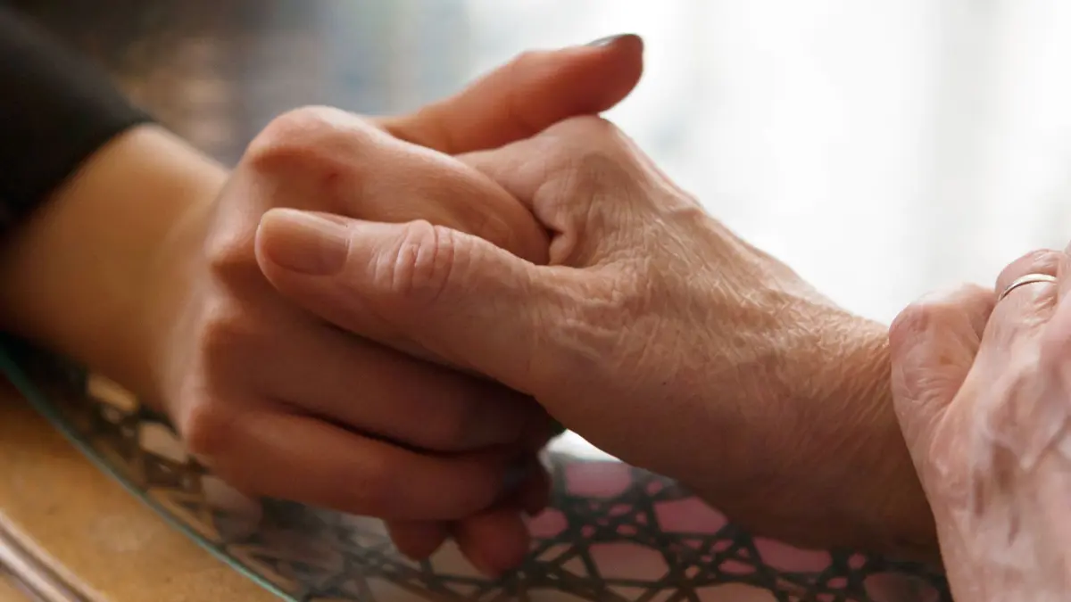 Frau und ihre Mutter halten sich an den Händen: ILLUSTRATION - Weil man seine Angehörigen im Alter gut versorgt wissen will, ist es gut, wenn Pflege kein Tabuthema ist. (zu dpa: «Miteinander reden: Damit eine Pflege gut vorbereitet ist») Foto: Silvia Marks/dpa-tmn - Honorarfrei nur für Bezieher des dpa-Themendienstes +++ dpa-Themendienst +++