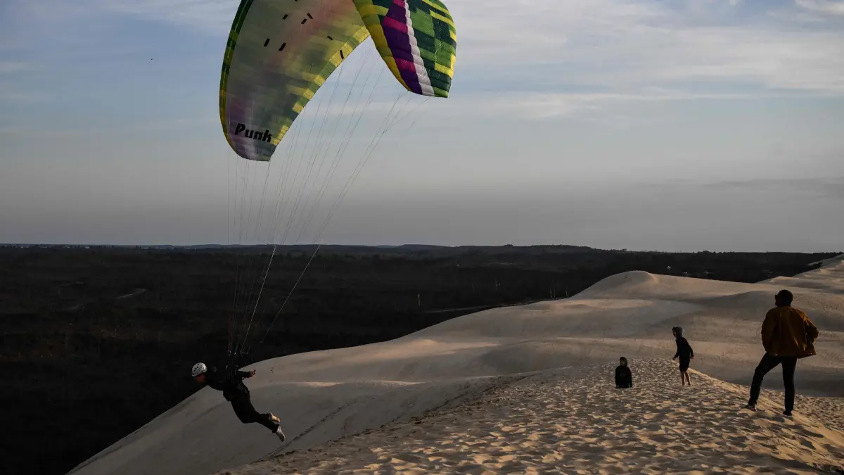 -: A pilot practices paragliding over the Dune of Pilat, the tallest sand dune in Europe, in Pyla-sur-Mer, La Teste-de-Buch, southwestern France, on March 4, 2025. The Dune of Pilat, one of Europe's largest, constantly shifts due to wind and tides, acting as a natural barrier that protects the coastline and the Landes forest from erosion while remaining vulnerable to the same forces. (Photo by Philippe LOPEZ / AFP)