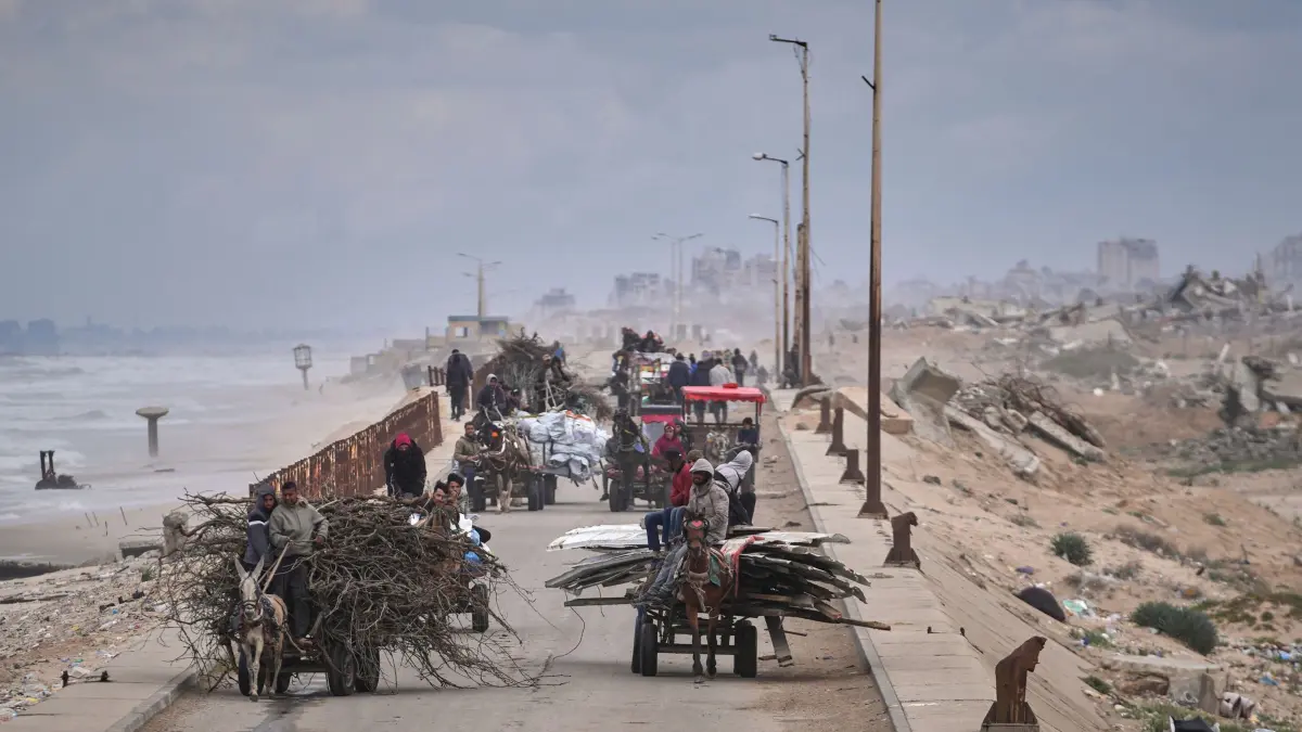 Nahostkonflikt - Gazastreifen: 21.03.2025, Palästinensische Gebiete, Gaza: Vertriebene Palästinenser, die ihre Habseligkeiten, Holz und andere Gegenstände mit sich führen, bewegen sich zwischen dem südlichen und dem nördlichen Gazastreifen entlang einer Strandstraße abseits der Gebiete, in denen die israelische Armee nach der erneuten israelischen Offensive im Gazastreifen operiert: Foto: Abdel Kareem Hana/AP/dpa +++ dpa-Bildfunk +++