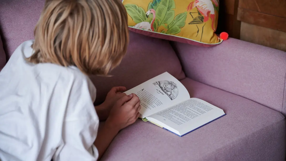 Kind liest, während es auf der Couch liegt: ILLUSTRATION - Abtauchen in die Fiktion: Lesen hilft Kindern in ihrer Entwicklung. (zu dpa: «Wie Bücher Kinder stark machen: Tipps für Eltern») Foto: Annette Riedl/dpa/dpa-tmn - Honorarfrei nur für Bezieher des dpa-Themendienstes +++ dpa-Themendienst +++