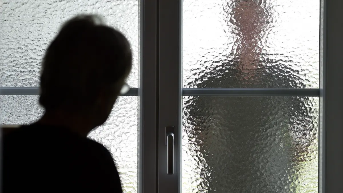 ILLUSTRATION - Eine Frau steht an einer Glasscheibe, hinter der ein Stalker steht. (gestellte Szene). (zu dpa «Hessen macht sich für verschärftes Gesetz gegen Stalking stark») +++ dpa-Bildfunk +++