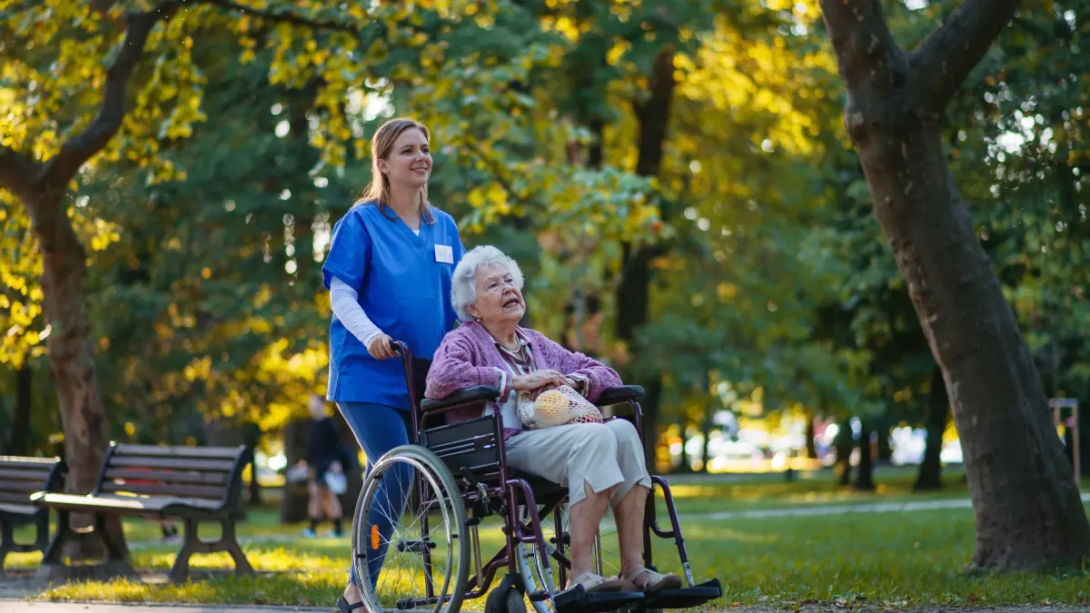Smiling healthcare worker walking with senior woman sitting in wheelchair at park model released, Symbolfoto, HAPF03393: Smiling healthcare worker walking with senior woman sitting in wheelchair at park model released, Symbolfoto, HAPF03393