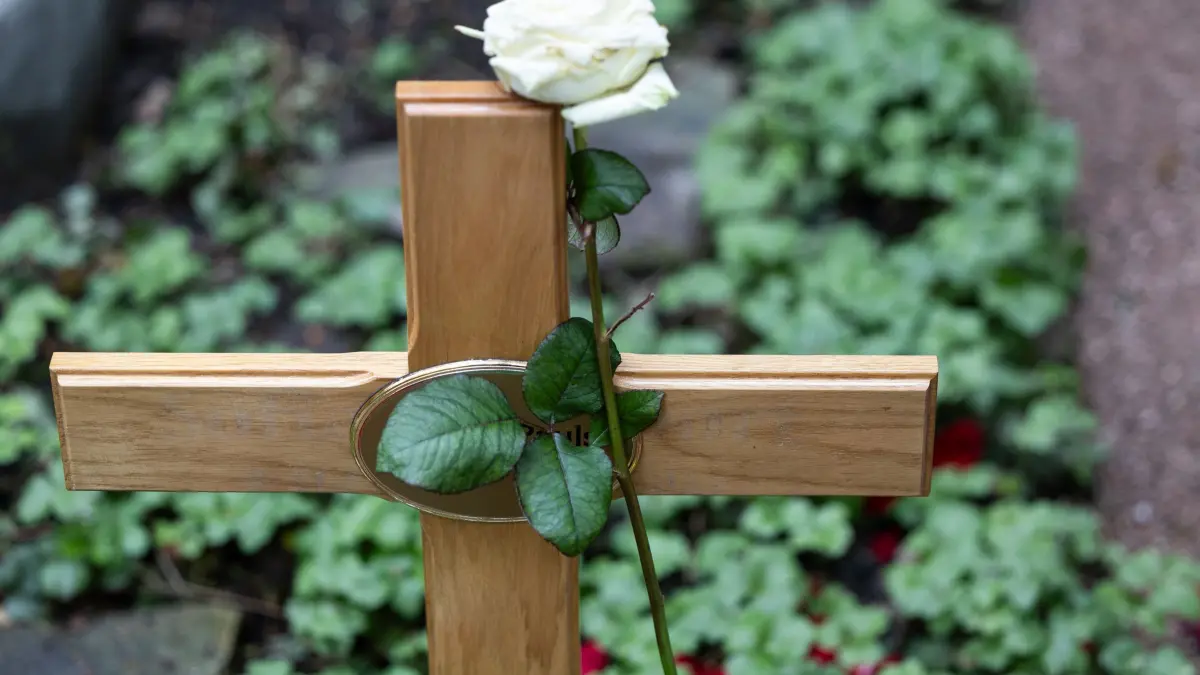 Symbolbild - Beerdigung: ARCHIV - 12.04.2024, Hessen, Frankfurt/Main: Blick auf ein frisches Grab mit Holzkreuz, an dem eine weiße Rose lehnt. (zu dpa: «Bestatter wollen mehr Qualität im Handwerk») Foto: Hannes P Albert/dpa +++ dpa-Bildfunk +++