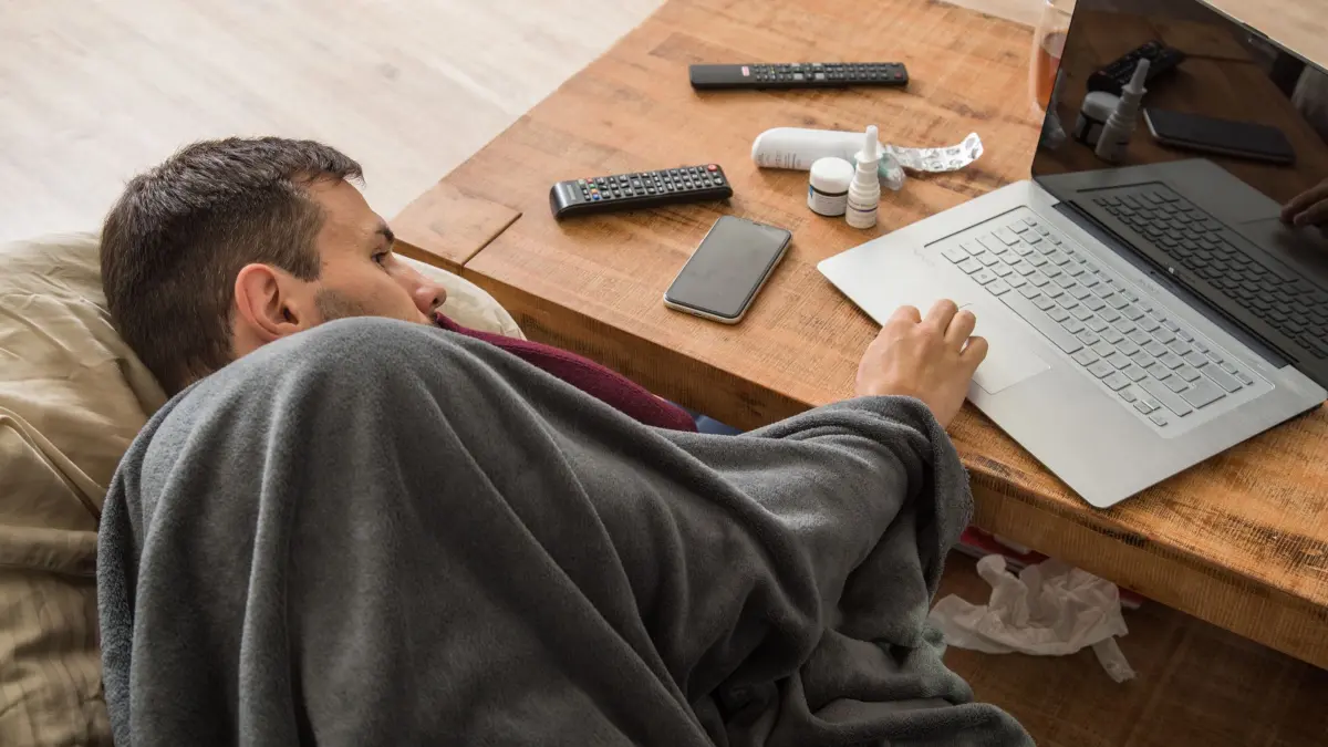 Ein Mann liegt krank auf dem Sofa: ILLUSTRATION - Chatbots bei Symptomen zu befragen ist zwar praktisch, kann jedoch keinen Arztbesuch ersetzen. (zu dpa: «Symptome per KI checken - aber nur mit Kontrolle») Foto: Christin Klose/dpa-mag - Honorarfrei nur für Bezieher des Dienstes dpa-Magazin +++ dpa-Magazin +++