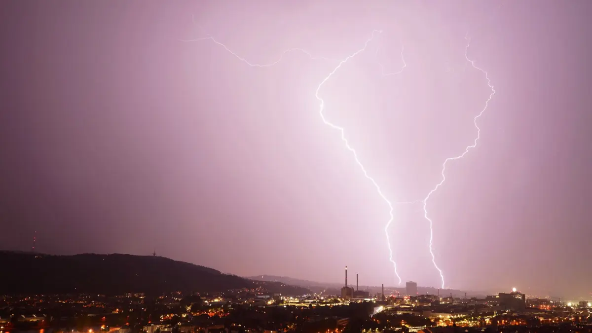ARCHIV - 24.08.2023, Baden-Württemberg, Stuttgart: Zwei Blitze entladen sich während eines Gewitters hinter dem Gaskessel in Stuttgart. Der Deutsche Wetterdienst (DWD) erwartet Gewitter und teils heftigen Starkregen in Baden-Württemberg. (zu dpa: «Bilanz: Weniger Blitze im Südwesten eingeschlagen») Foto: Andreas Rosar/dpa +++ dpa-Bildfunk +++