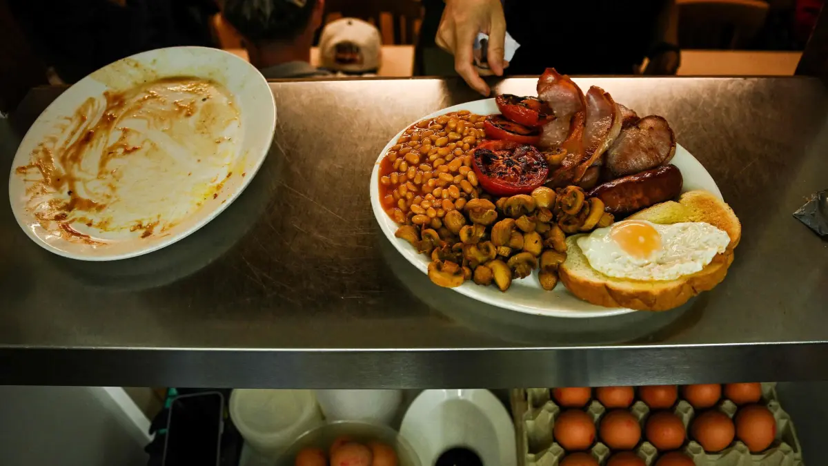 A member of staff picks up a full English breakfast to serve customers at the Italian family run cafe E. Pellicci, in east London, on June 3, 2025. Opened 125 years ago by Anna Pellicci’s grandparents, the family-owned and run cafe E. Pellicci went from being the breakfast place of the gangsters the Kray brothers to an East End institution where cockney accent meets Italian heritage with customers coming from the neighbourhood but also from all over the word.
“The menu has changed a bit, before it was only British, but with time we have introduced some Italian recipes, but not too much. As we say : ain’t broken don’t fix it” explained Anna Pellici who manages the restaurant with her brother Nevio. “We start preparing the food at 7am, before with my husband it was 4am” told Maria Pellici. A bit after 7:30 Nevio’s daughters and wife arrive for breakfast “When we were little we would come here every morning for breakfast and every evening for dinner with all the family.” remembered Nevio and Anna. On the wall pictures of the grandparents and the whole family are displayed. “Nonna (granny in english) started to buy one panel of wood at a time in 1946 from an Italian artisan living here behind Achille Capacci, now they are listed by the English Heritage”. Once the doors open at 8am its a bustle of customers. Michelle 39, lives in the neighbourhood “I used to come here everyday when i was living next door, now a bit less. I love this place there is a feeling of family”. (Photo by Ben STANSALL / AFP)
