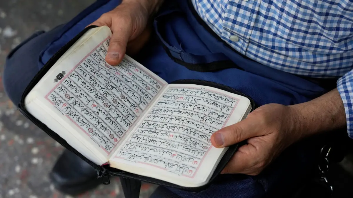 Nahostkonflikt -Teheran: 20.06.2025, Iran, Teheran: Ein Mann liest den Koran, das heilige Buch der Muslime, vor Beginn einer Demonstration zur Verurteilung israelischer Angriffe auf mehrere Städte im Iran. Foto: Vahid Salemi/AP/dpa +++ dpa-Bildfunk +++