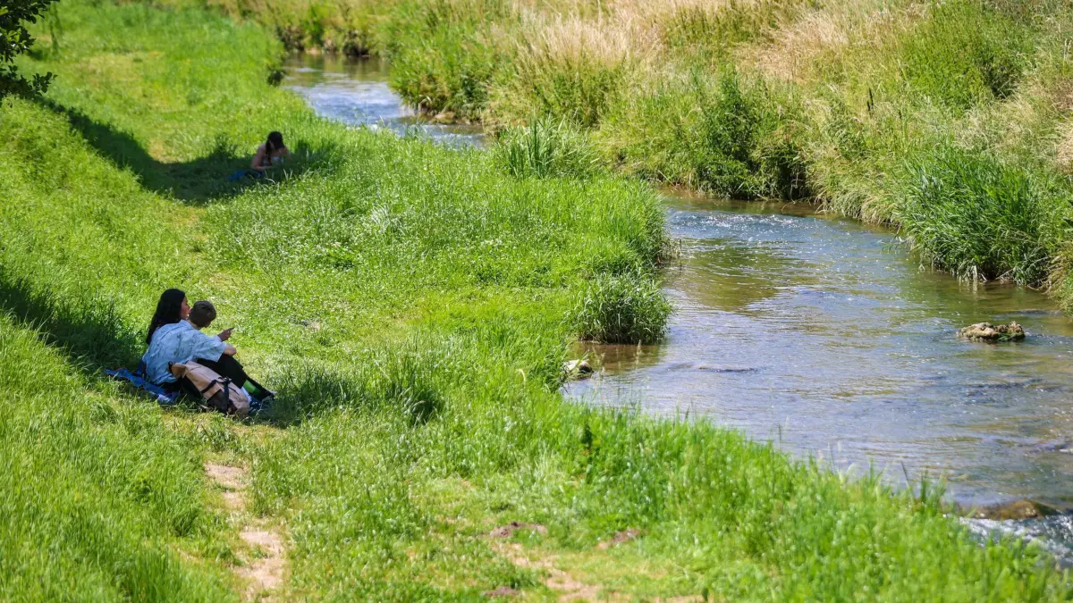 Sommerwetter in Baden-Württemberg: 21.06.2024, Baden-Württemberg, Tübingen: Menschen sitzen an der Ammer im Schatten von Bäumen und genießen das Sommerwetter. Die Menschen im Land können sich auf ein sonniges Sommerwochenende mit Temperaturen bis zu 37 Grad am Sonntag freuen. Foto: Christoph Schmidt/dpa +++ dpa-Bildfunk +++