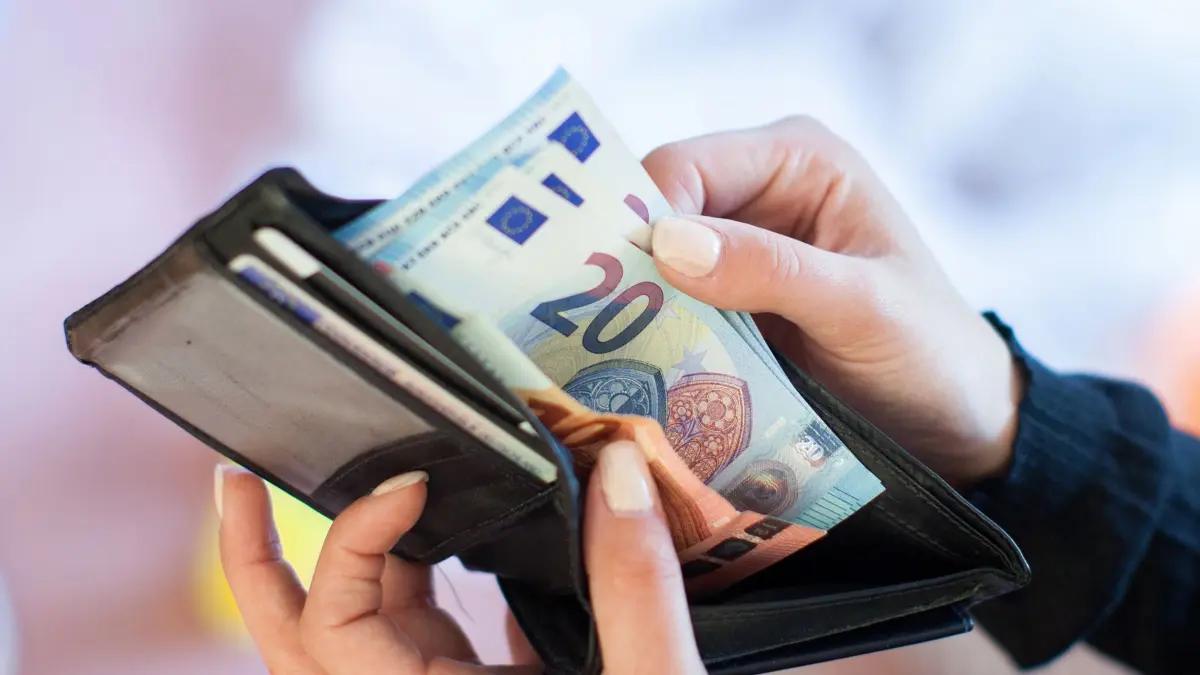 ILLUSTRATION - Eine Frau nimmt Banknoten aus einem Geldbeutel. Inflation, wirtschaftliche Unsicherheit, Kriege: Nach den schwierigen Pandemie-Jahren brachte auch 2023 für viele Menschen keinen spürbaren Aufschwung. Das Jahr war für Verbraucher nicht einfach. (Zu dpa "Was bleibt 2024 im Geldbeutel?") +++ dpa-Bildfunk +++