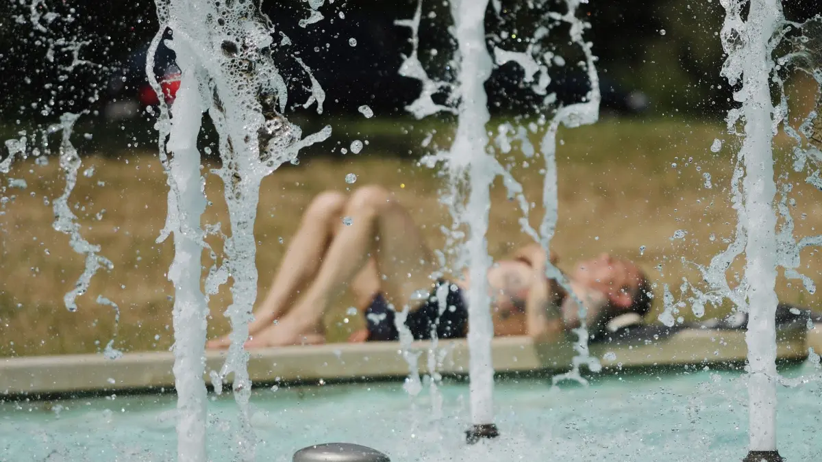 Sommerwetter in Sachsen: ARCHIV - 21.06.2025, Sachsen, Leipzig: Ein Mann sonnt sich am Rand eines Springbrunnens. Am Wochenende herrscht in Deutschland hochsommerliches Wetter vor. (zu dpa: «Hitzeschutzkonzept für Sächsische Schweiz und Osterzgebirge») Foto: Sebastian Willnow/dpa +++ dpa-Bildfunk +++