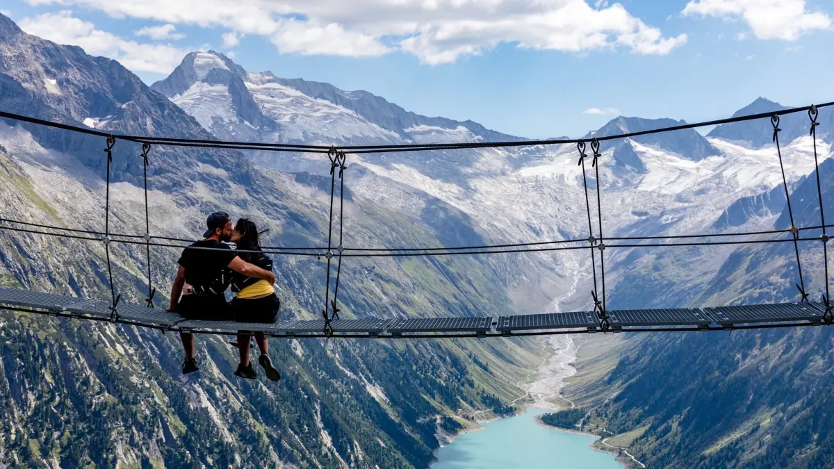 Foto-Hotspot in den Zillertaler Alpen: ARCHIV - 19.08.2023, Österreich, Zillertaler Alpen: Eine Frau und ein Mann küssen sich auf einer Hängebrücke an einem Wanderweg in den Zillertaler Alpen - mit Blick auf den Schlegeis-Speicher und die umgebenden Alpengipfel. (zu dpa: «Umfrage: Viele Österreicher sehen Tourismus positiv») Foto: Frank Hammerschmidt/dpa +++ dpa-Bildfunk +++