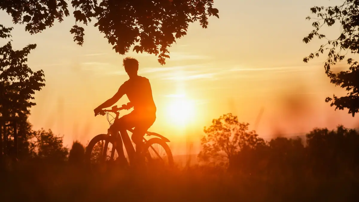 ARCHIV - 22.06.2025, Baden-Württemberg, Uttenweiler: Ein Radfahrer ist am Morgen unterwegs, während hinter ihm die Sonne aufgeht. (zu dpa: «So heiß wird es am Wochenende») Foto: Thomas Warnack/dpa +++ dpa-Bildfunk +++