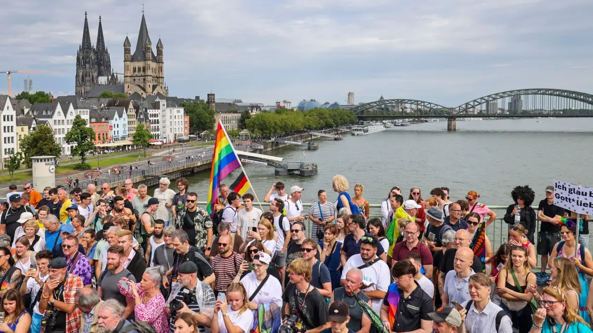 ColognePride – Parade zum Christopher Street Day (CSD): ARCHIV - 21.07.2024, Nordrhein-Westfalen, Köln: Eine Regenbogenflagge bei den Zuschauern beim CSD in Köln, im Hintergrund der Kölner Dom. Mit mehr als 60.000 Teilnehmern und über eine Million erwarteten Besuchern gilt der Kölner CSD als einer der größten in Europa. (zu dpa: «CSD-Demonstration zieht durch Köln») Foto: Christoph Reichwein/dpa +++ dpa-Bildfunk +++