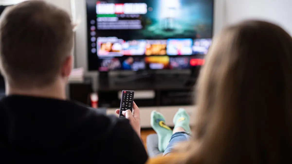 Paar sitzt vor einem Fernseher mit Streamingdiensten: ILLUSTRATION - Treue bei Streaming-Abos zahlt sich nicht unbedingt aus. Günstige Angebote gibt es oft, wenn man wechselt oder einen neuen Vertrag abschließt. (zu dpa: «Welche 7 Finanzfehler Sie vermeiden sollten») Foto: Daniel Reinhardt/dpa/dpa-tmn - Honorarfrei nur für Bezieher des dpa-Themendienstes +++ dpa-Themendienst +++