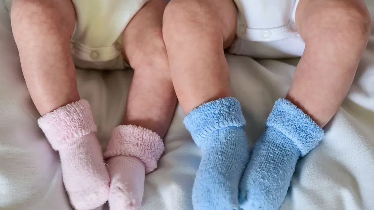Geburtenrate gesunken: ARCHIV - 14.04.2015, Brandenburg, Frankfurt (Oder): Rosa und blaue Söckchen für ein Mädchen und einen Jungen und die nackten Babybeine von Zwillingen, aufgenommen in einem Babybettchen. (zu dpa: «Geburtenrate sinkt auf 1,35 Kinder je Frau») Foto: Patrick Pleul/dpa-Zentralbild/dpa +++ dpa-Bildfunk +++