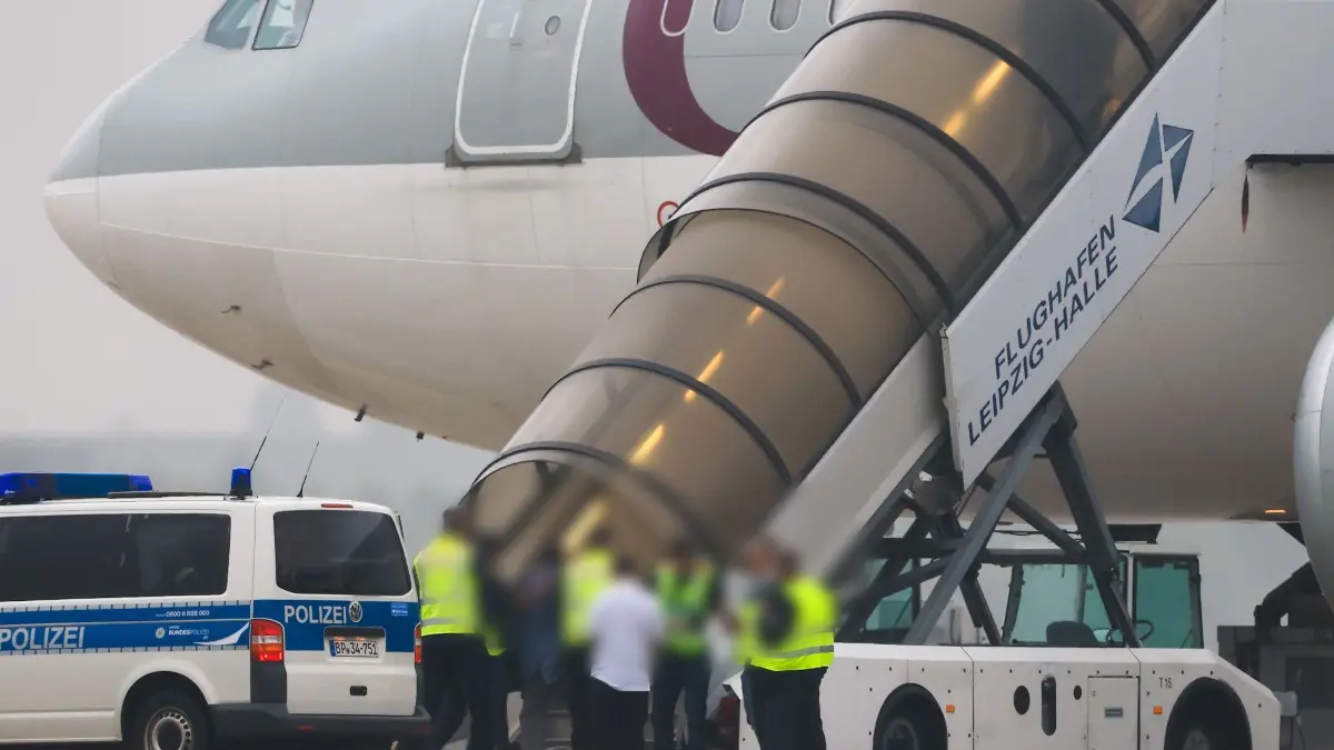 Flughafen Leipzig: 18.07.2025, Sachsen, Schkeuditz: Menschen besteigen ein Flugzeug der Qatar Airways, vor dem Fahrzeuge der Bundespolizei stehen auf dem Vorfeld am Flughafen Leipzig/Halle. Foto: Jan Woitas/dpa - ACHTUNG: Person(en) wurde(n) aus rechtlichen Gründen gepixelt +++ dpa-Bildfunk +++