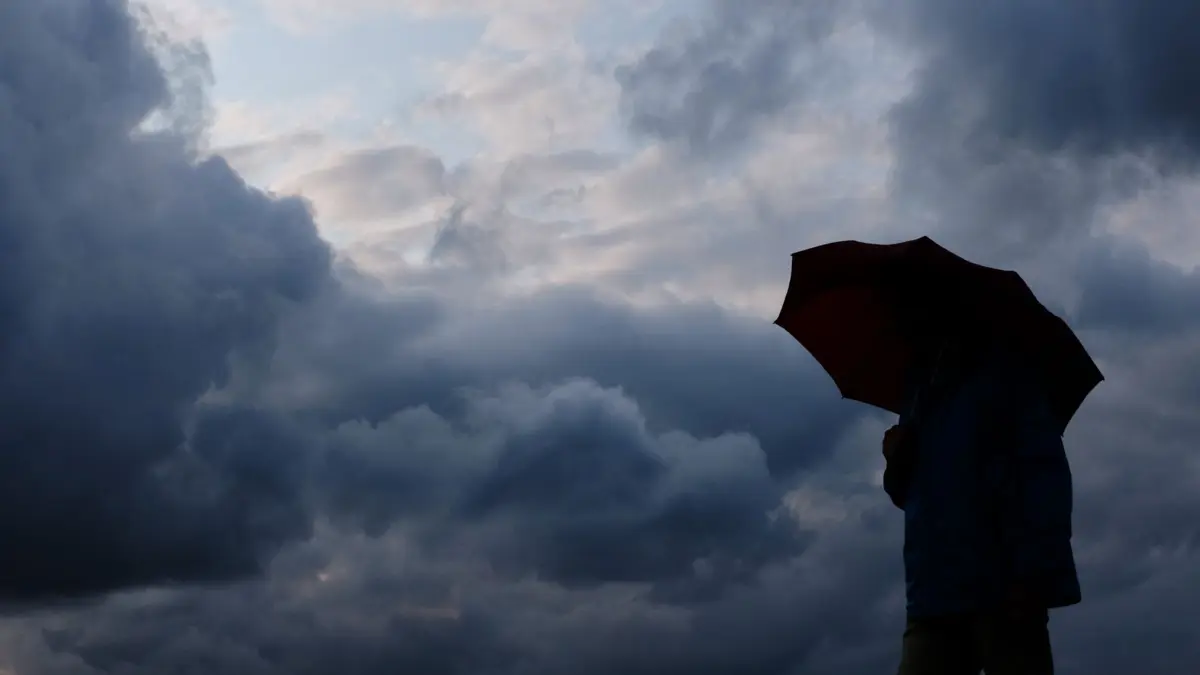 ARCHIV - 12.07.2019, Nordrhein-Westfalen, Duisburg: Ein Mann geht mit einem Regenschirm vor aufziehenden dunklen Wolken spazieren. (zu dpa: «Regen, Wolken und Gewitter in Nordrhein-Westfalen erwartet») Foto: Martin Gerten/dpa +++ dpa-Bildfunk +++