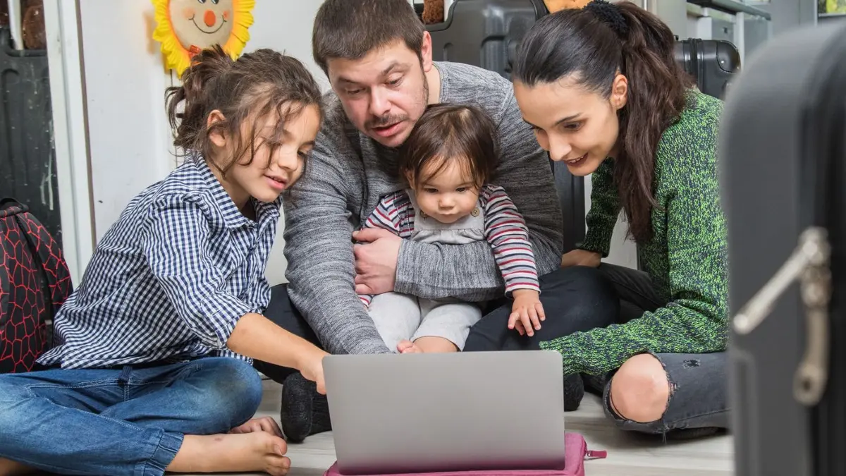Familie plant mit Laptop ihren Urlaub: ILLUSTRATION - Was muss alles in den Koffer? KI-Tools können dabei helfen, spezifische Packlisten zu erstellen. (zu dpa: «Künstliche Intelligenz hilft beim Kofferpacken») Foto: Christin Klose/dpa-mag - ACHTUNG: Nur zur redaktionellen Verwendung im Zusammenhang mit dem genannten Text - Honorarfrei nur für Bezieher des Dienstes dpa-Magazin +++ dpa-Magazin +++