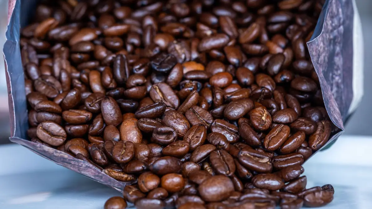 Kaffee: SYMBOLBILD - 02.04.2025, Mecklenburg-Vorpommern, Pokrent: Geröstete Kaffeebohnen liegen vor einer Tüte. (zu dpa: «Kaffeediebe stehlen Hunderte Packungen aus Supermärkten») Foto: Jens Büttner/dpa +++ dpa-Bildfunk +++