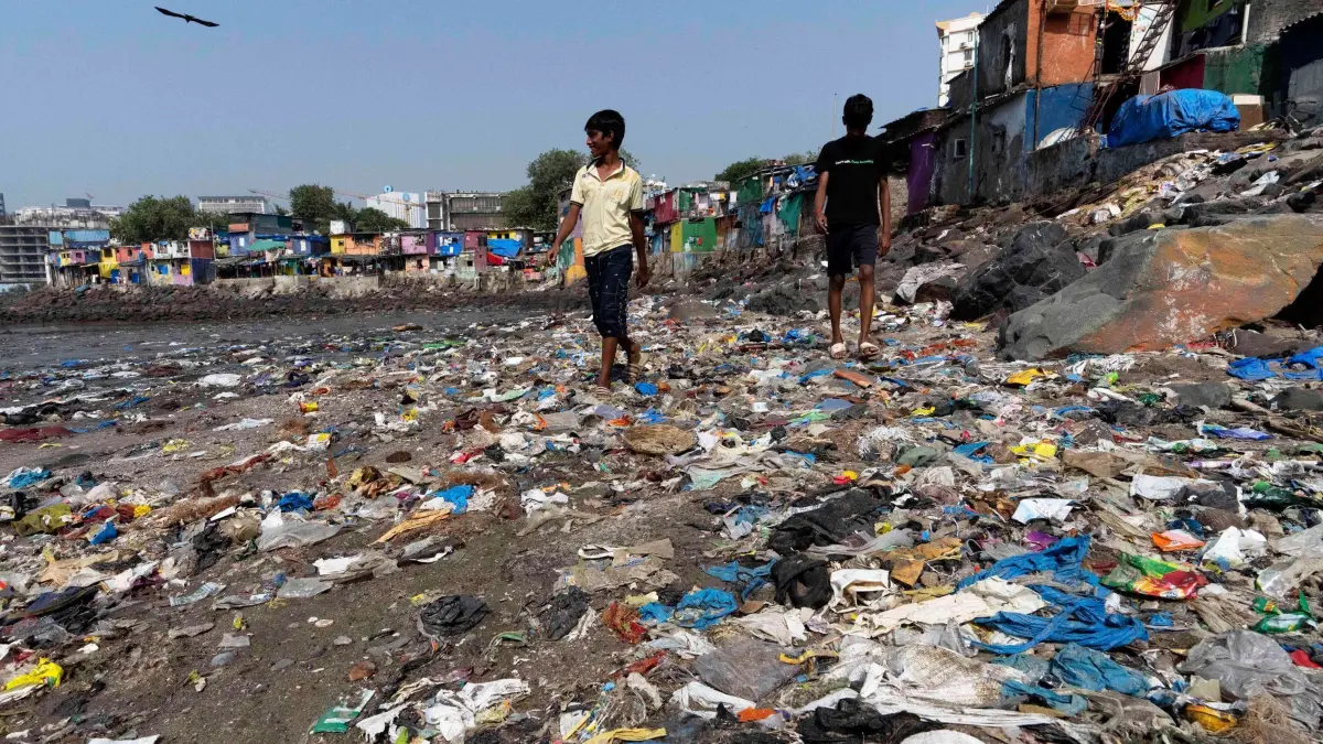 Verhandlungen über globalen Vertrag gegen Plastikverschmutzung: ARCHIV - 26.11.2024, Indien, Mumbai: Menschen spazieren am Strand des Badhwar Park an der Küste des Arabischen Meeres an Plastikmüll vorbei. (zu dpa: «Letzte Chance: Verhandlungen über UN-Plastik-Abkommen») Foto: Rajanish Kakade/AP/dpa +++ dpa-Bildfunk +++