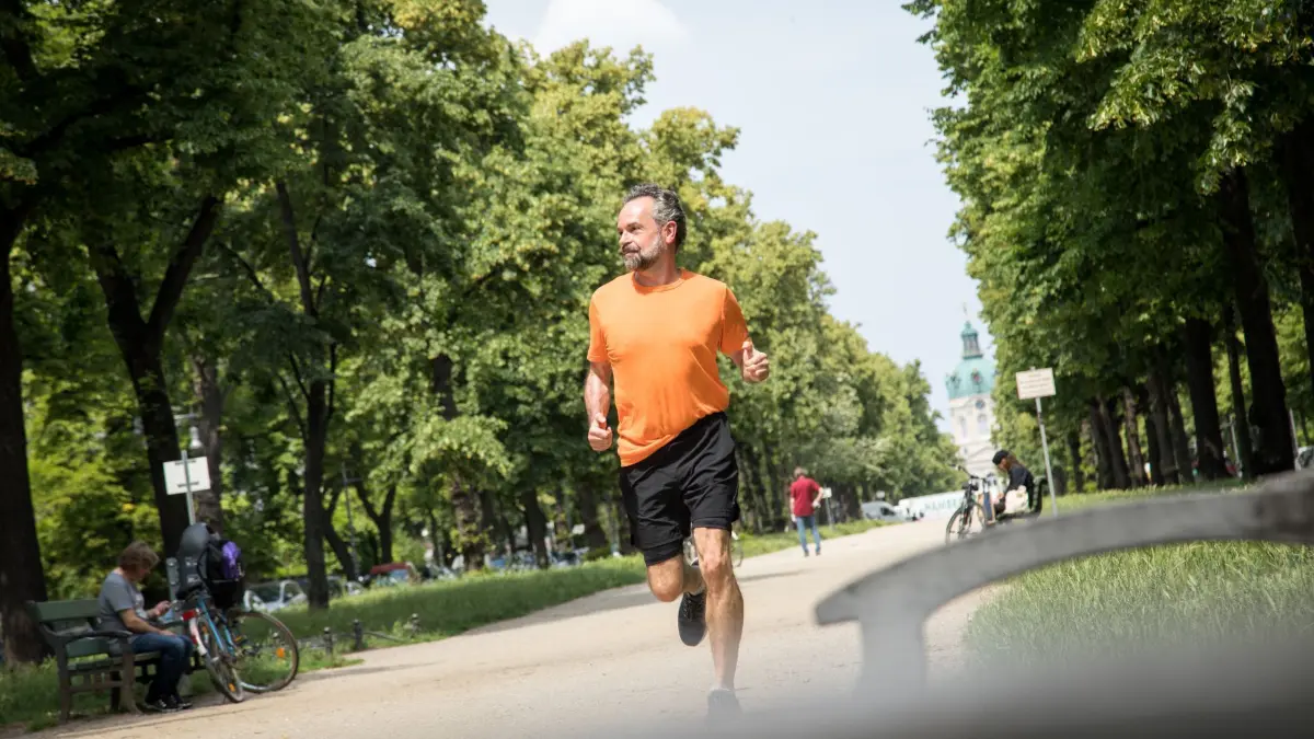 Ein Mann joggt durch einen Park: ILLUSTRATION - Sportliche Aktivitäten bei hohen Temperaturen sollten reduziert und zeitlich angepasst werden. (zu dpa: «5 Tipps für die Hitzetage») Foto: Christin Klose/dpa-tmn - Honorarfrei nur für Bezieher des dpa-Themendienstes +++ dpa-Themendienst +++