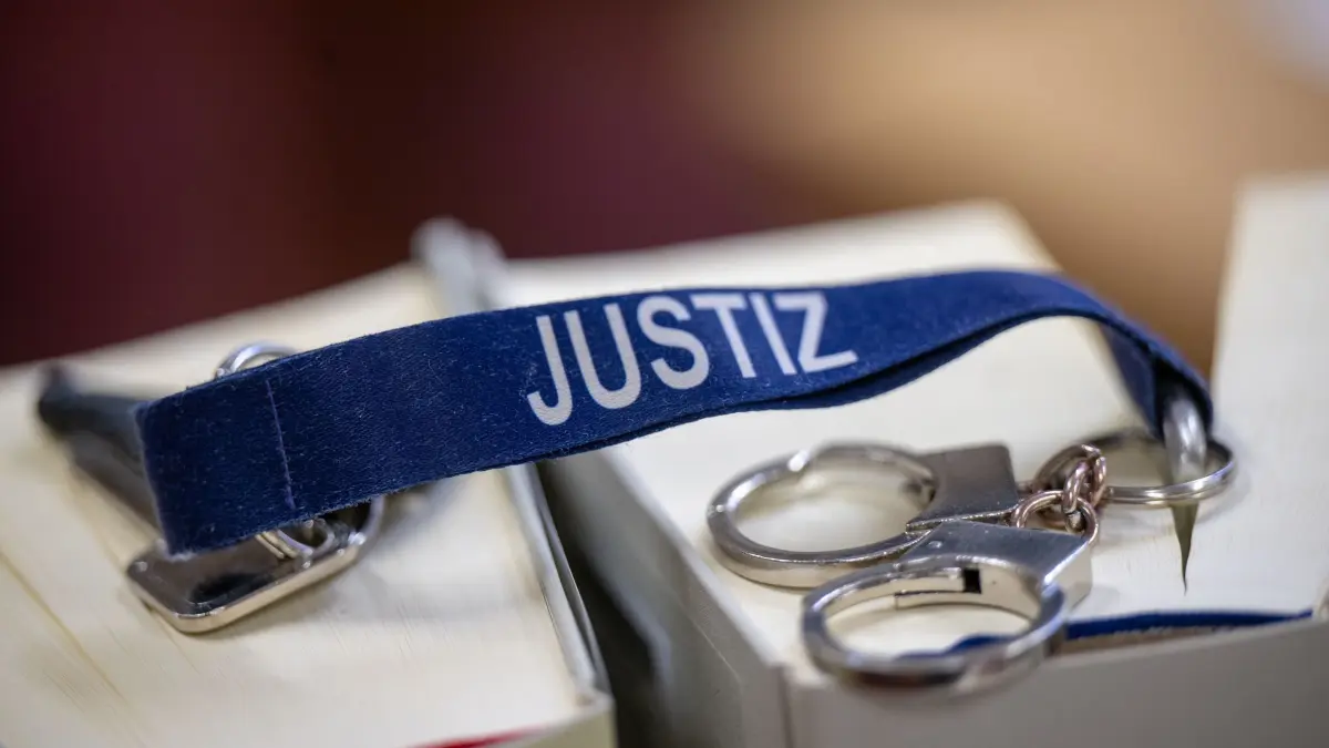 Justiz: ARCHIV - 27.03.2024, Berlin: Ein Schlüsselanhänger mit dem Wort «Justiz» und Mini-Handschellen liegen auf zwei Gesetzbüchern im Büro einer Richterin im Kriminalgericht Moabit. (zu dpa: «Unliebsamen Untermieter überfallen: Angeklagter gesteht») Foto: Monika Skolimowska/dpa +++ dpa-Bildfunk +++