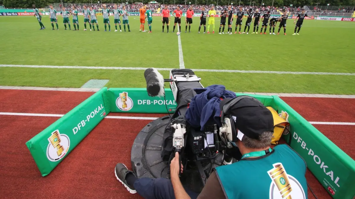Marschweg-Stadion Oldenburg: ARCHIV - 08.08.2021, Niedersachsen, Oldenburg: Fußball, DFB-Pokal, 1. Runde, Saison 2021/22, VfL Oldenburg - Fortuna Düsseldorf im Marschweg-Stadion. Ein TV-Kameramann bei der Arbeit während die Mannschaften auflaufen. WICHTIGER HINWEIS: Gemäß den Vorgaben der DFL Deutsche Fußball Liga bzw. des DFB Deutscher Fußball-Bund ist es untersagt, in dem Stadion und/oder vom Spiel angefertigte Fotoaufnahmen in Form von Sequenzbildern und/oder videoähnlichen Fotostrecken zu verwerten bzw. verwerten zu lassen. (zu dpa: «Warum die Kleinen im Pokal oft kein echtes Heimspiel haben») Foto: Piet Meyer/dpa +++ dpa-Bildfunk +++