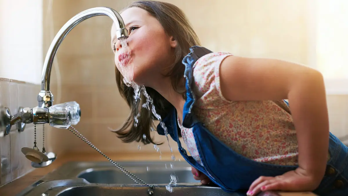 Shot of a little girl drinking water directly from the kitchen tap at home.