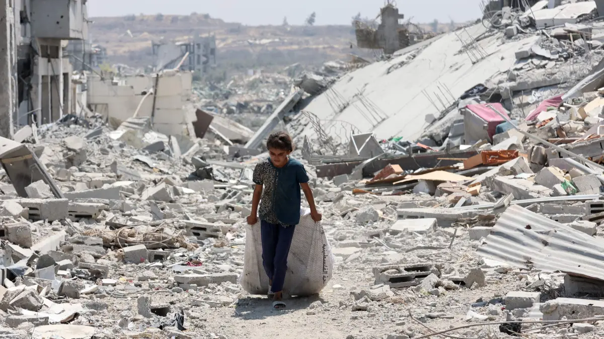 A Palestinian girl transports salvaged items next to destroyed buildings in the al-Tuffah neighbourhood of Gaza City on August 14, 2025, following more than 22 months of war between Israel and the Palestinian militant group Hamas. The Israeli military said on August 13, that it had approved the framework for a new offensive in the Gaza Strip, as Hamas condemned what it called "aggressive" Israeli ground incursions in Gaza City. The approved plan for the expanded offensive comes days after Israel's security cabinet called for the capture of the Palestinian territory's largest city following 22 months of war that have created dire humanitarian conditions. (Photo by Omar AL-QATTAA / AFP)