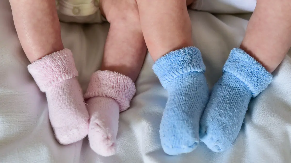 ILLUSTRATION - Rosa und blaue Söckchen für ein Mädchen und einen Jungen und die nackten Babybeine von Zwillingen, aufgenommen in einem Babybettchen. Weltweit werden einer Studie zufolge mehr Zwillinge geboren als je zuvor. (zu dpa: «Studie: Zahl der Zwillingsgeburten weltweit auf Rekordstand») +++ dpa-Bildfunk +++